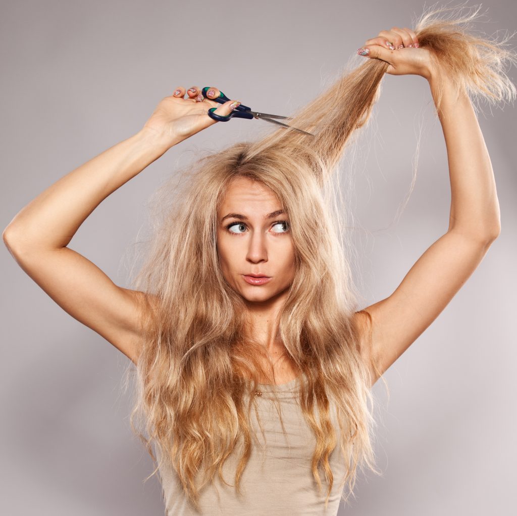 blonde woman with scissors thinking about cutting her hair