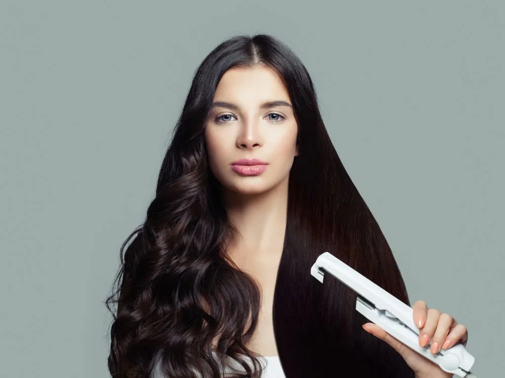 woman curling her hair with a flat iron