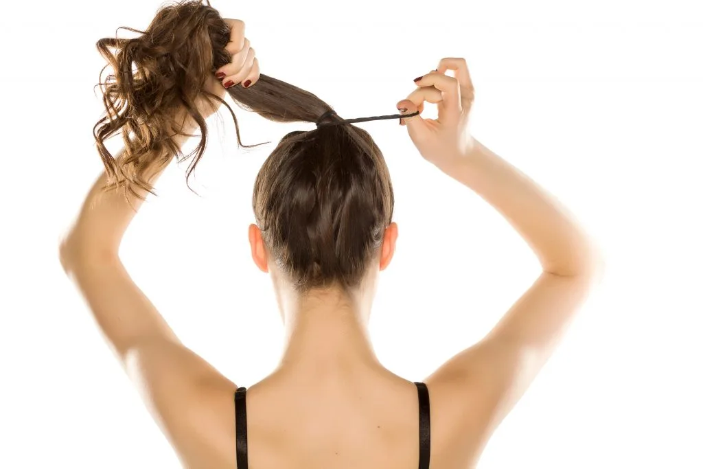 woman tying her hair in a ponytail