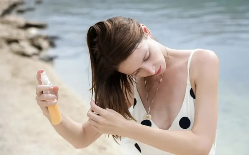 vrouw die zonnebeschermingsspray op haar haar doet