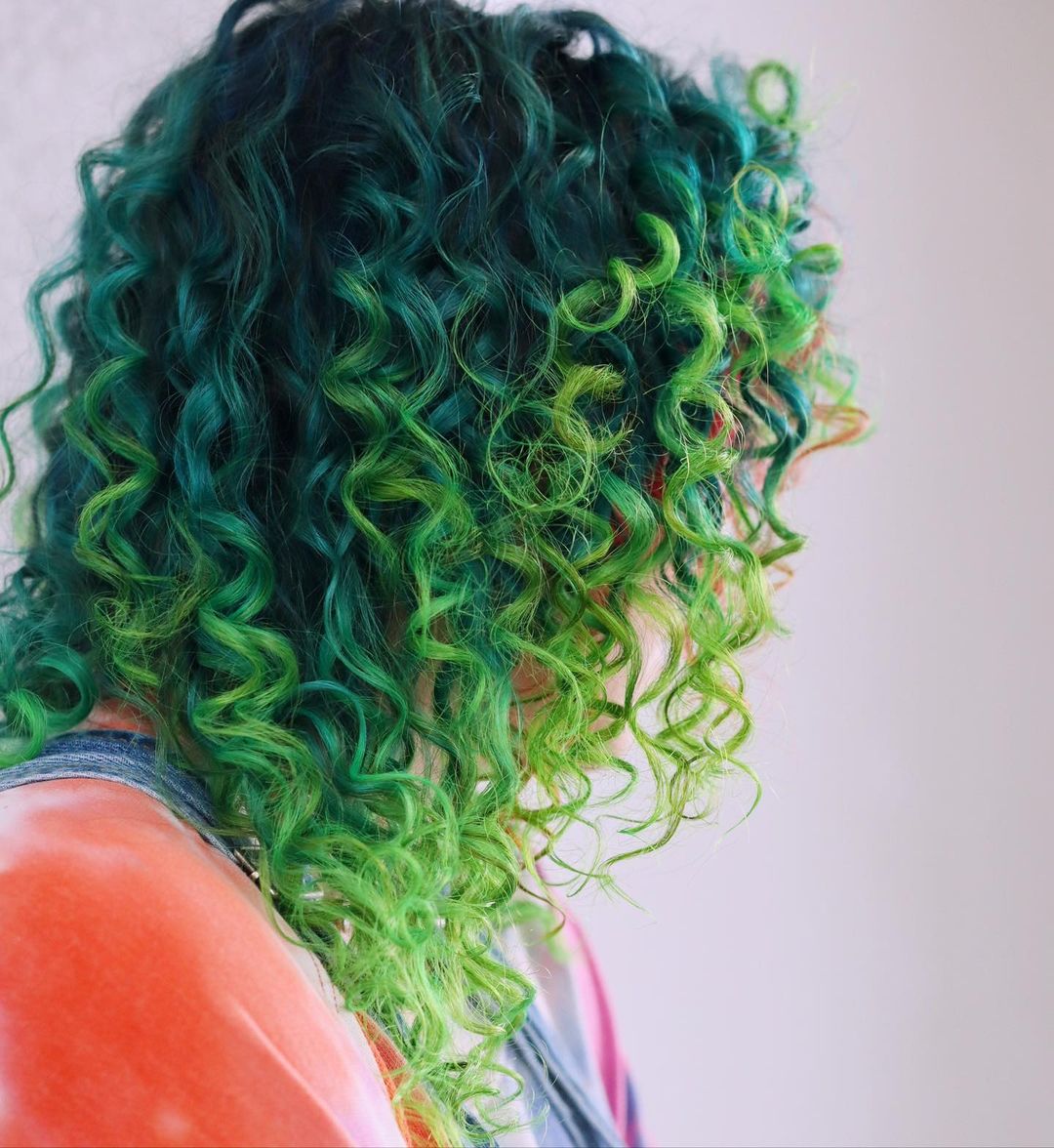 a woman with a mid length vibrant turquoise and lime green curls 