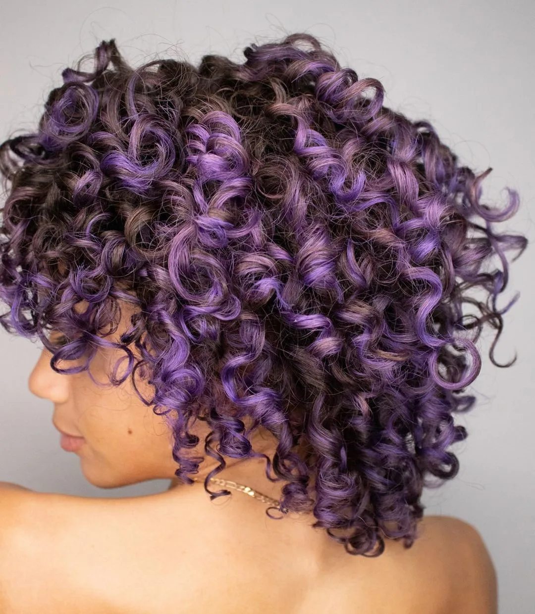 a woman with shoulder length brown curly hair and pastel purple highlights