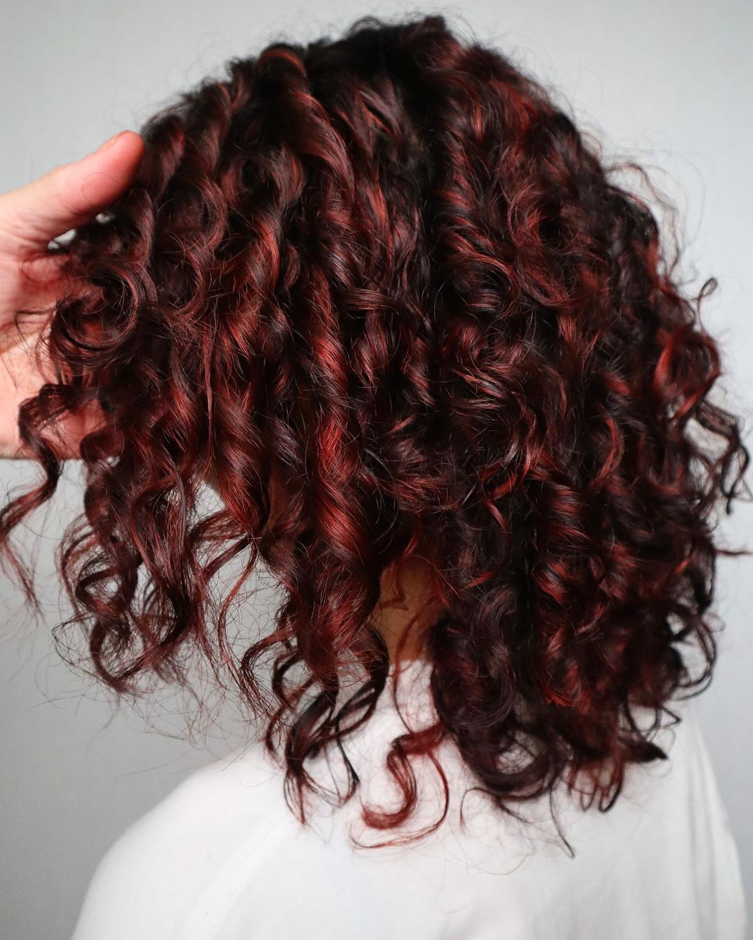 cabelo encaracolado na altura dos ombros com madeixas vermelhas mostrado por trás