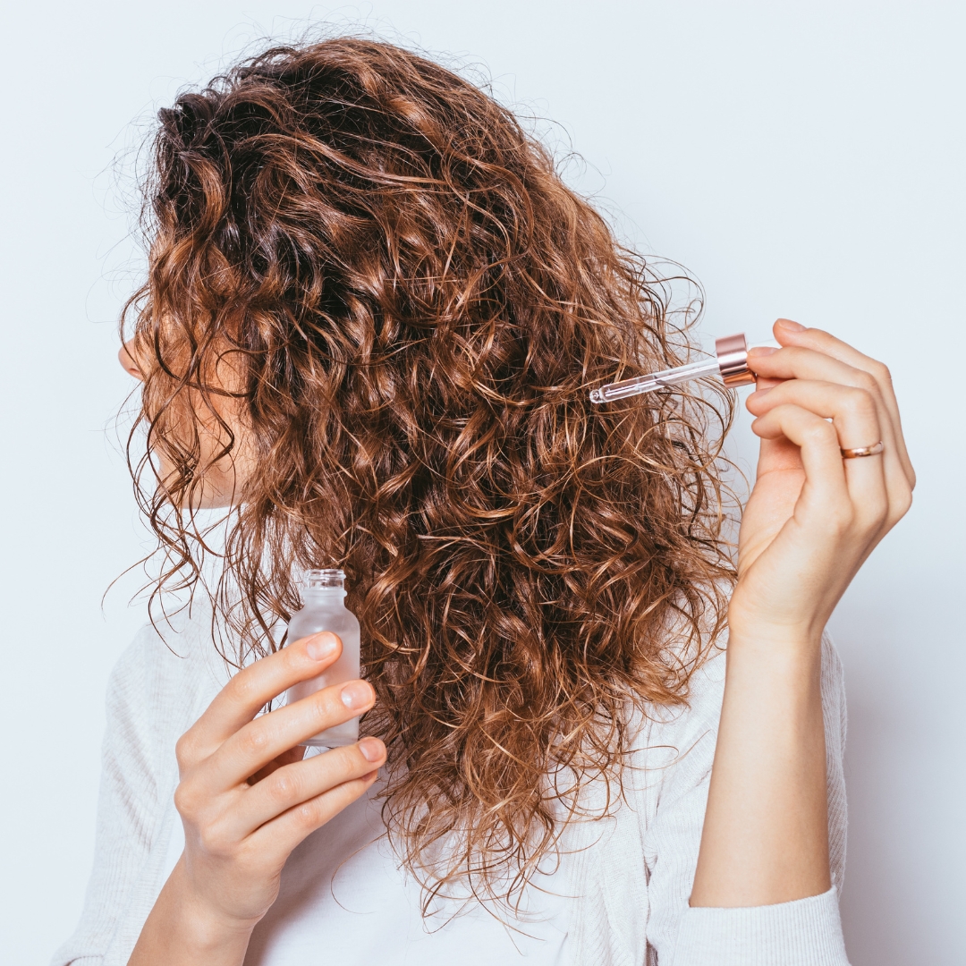 uma mulher a aplicar óleo no seu cabelo encaracolado 