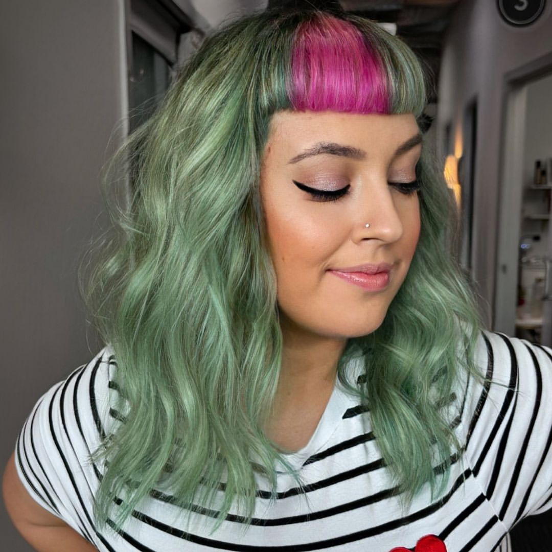 una donna con capelli mossi verde pastello rosa e micro frangia
