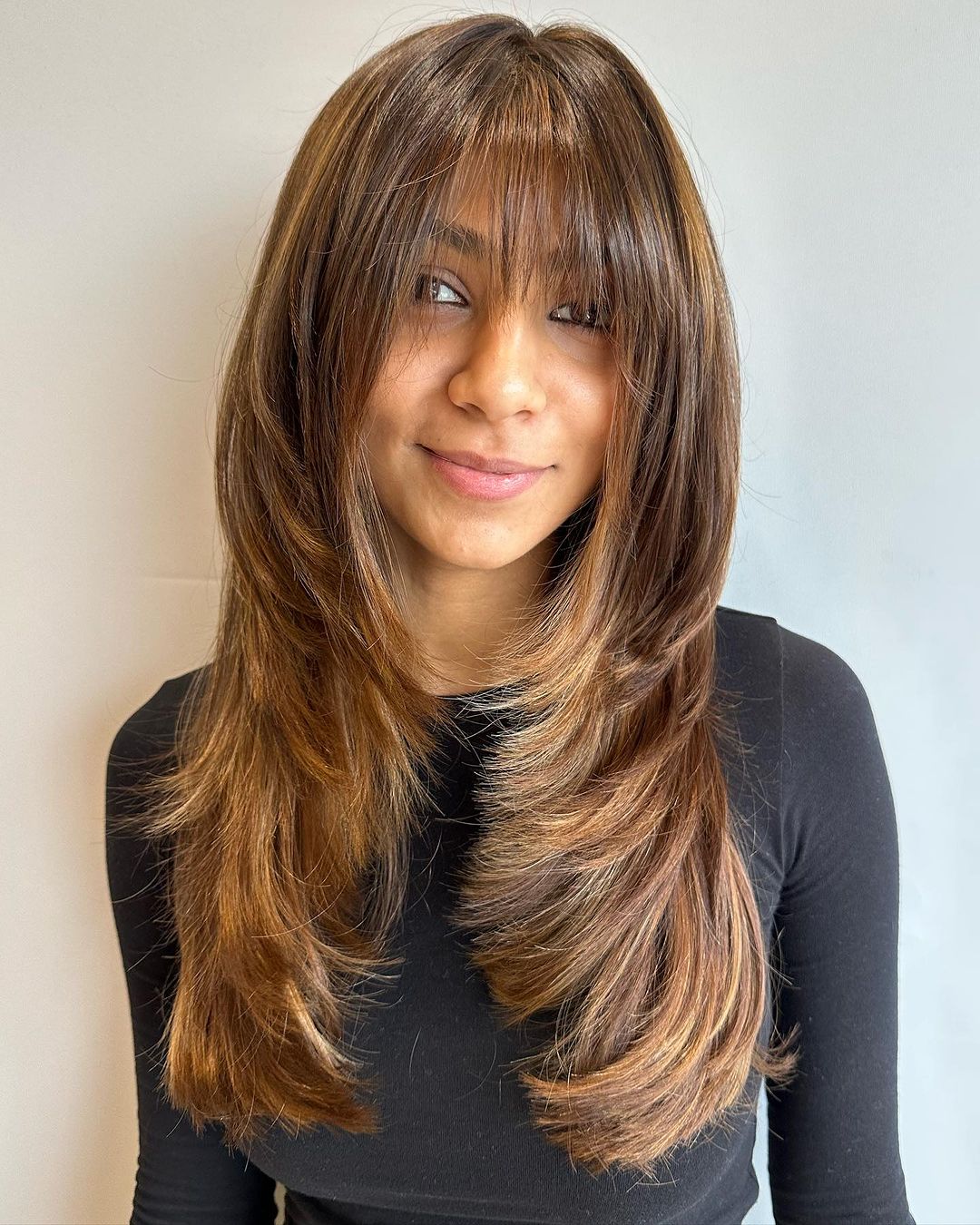 long layered hair with caramel highlights and wispy bangs