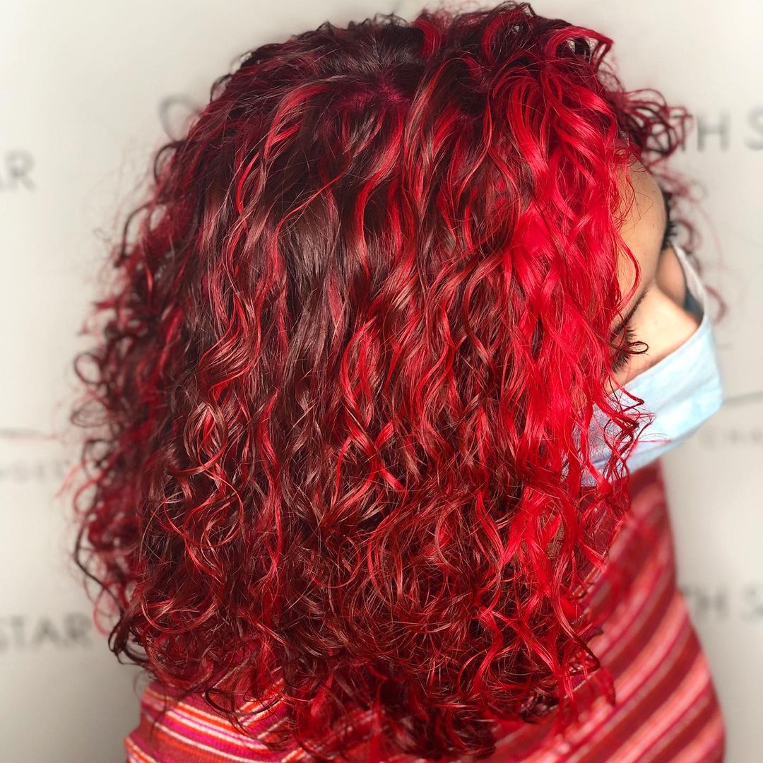 intense red money piece on brown curly hair with red highlights