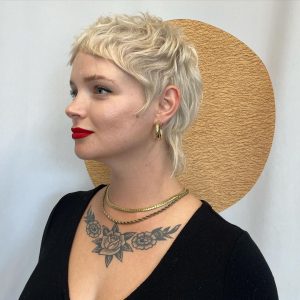 A blonde elf crop haircut showing short, uneven layers throughout the hairstyle, creating a naturally tousled, textured look that frames the face.