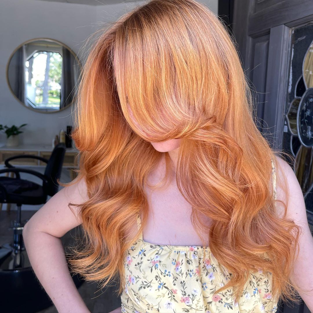 light copper strawberry blonde waves with curtain bangs