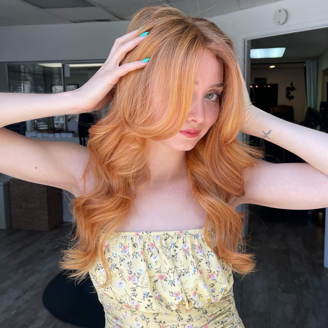 light copper strawberry blonde waves with curtain bangs