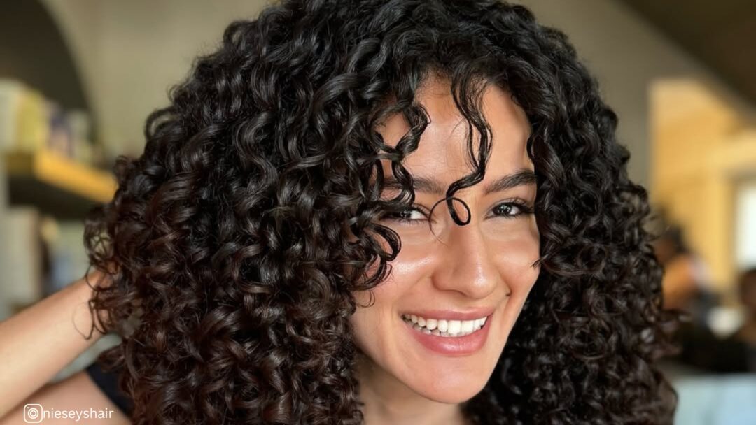 A side profile of a woman with layered curls that cascade down her back, highlighting the transformation